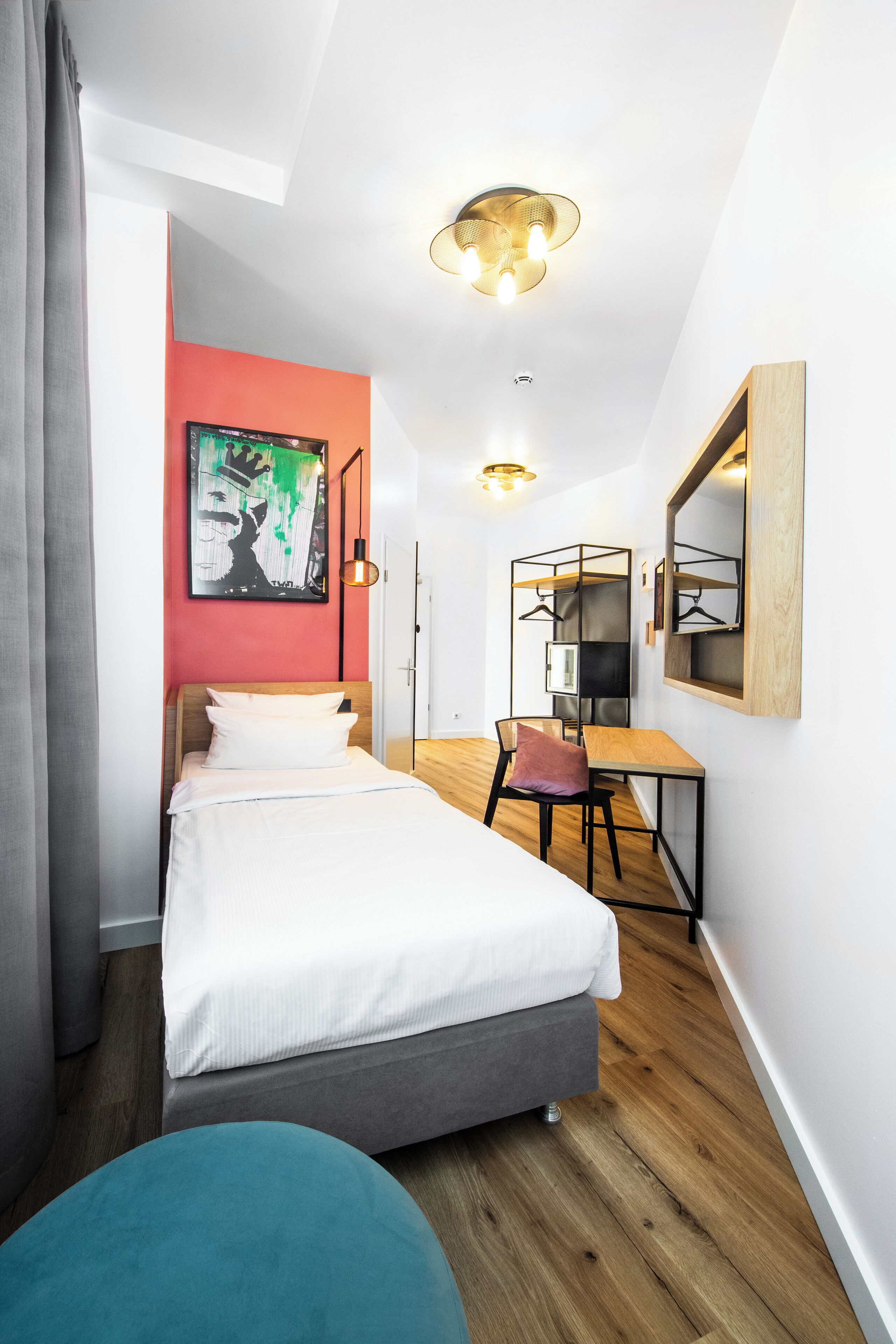Une chambre d’hôtel moderne, équipée d’un lit, d’un bureau et d’une chaise. Un tableau est accroché au mur et un miroir se trouve au-dessus du bureau.