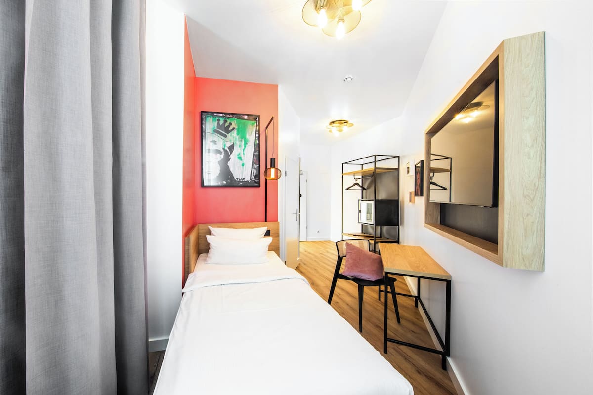 A hotel room with a bed, a desk, a chair, a mirror, and a wardrobe.