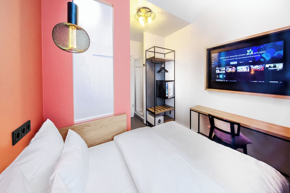 A hotel room with a bed, a TV mounted on the wall, a desk, and a wardrobe.