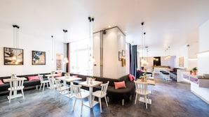 A modern interior with a mix of seating areas, including a black sofa and white tables with chairs. - CALMA Berlin Mitte (Berlin)