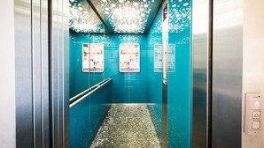 An elevator with teal walls, a patterned ceiling, and a metallic floor. - CALMA Berlin Mitte (Berlin)