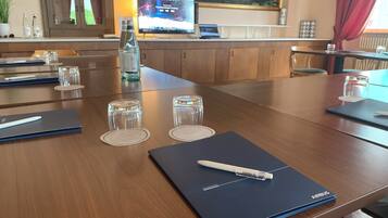 Un salón de conferencias con una mesa de madera, vasos de vidrio con agua, una computadora portátil y una tableta.