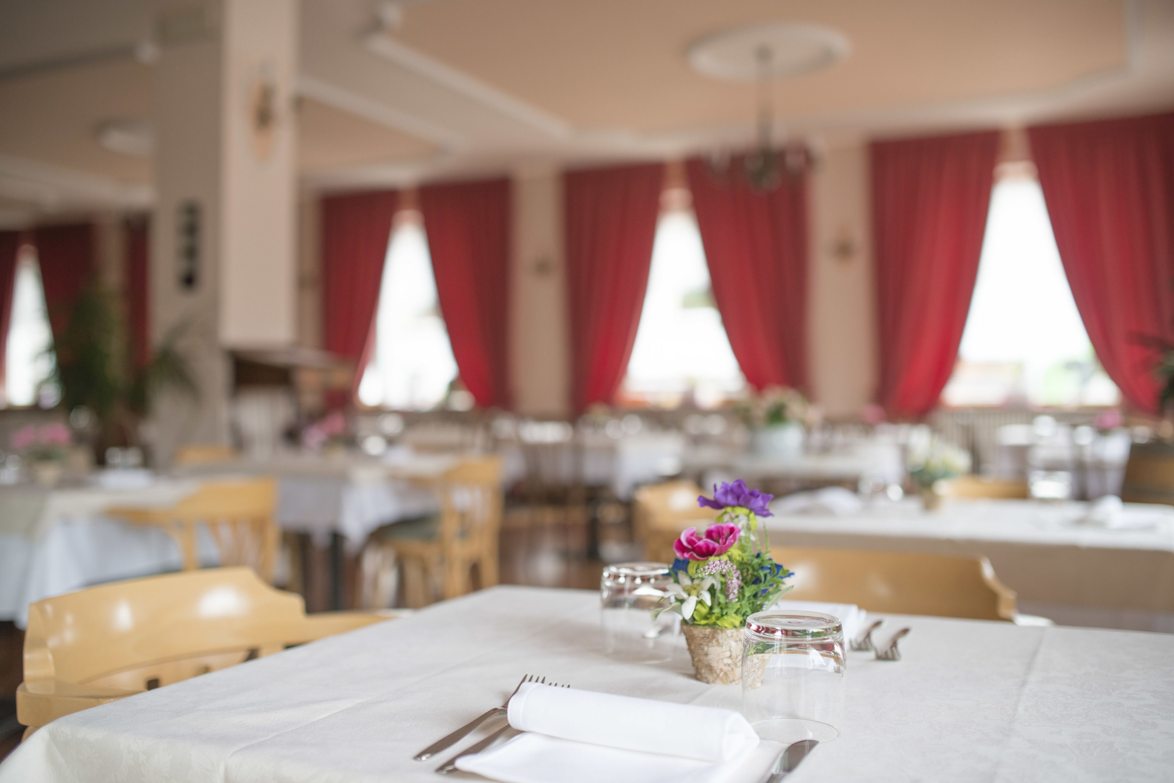 A dining area with tables set for service, red curtains, and a floral centerpiece.