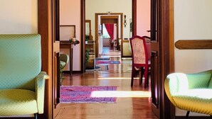 Un pasillo con piso de madera que conduce a una habitación con una silla roja y un sofá verde.