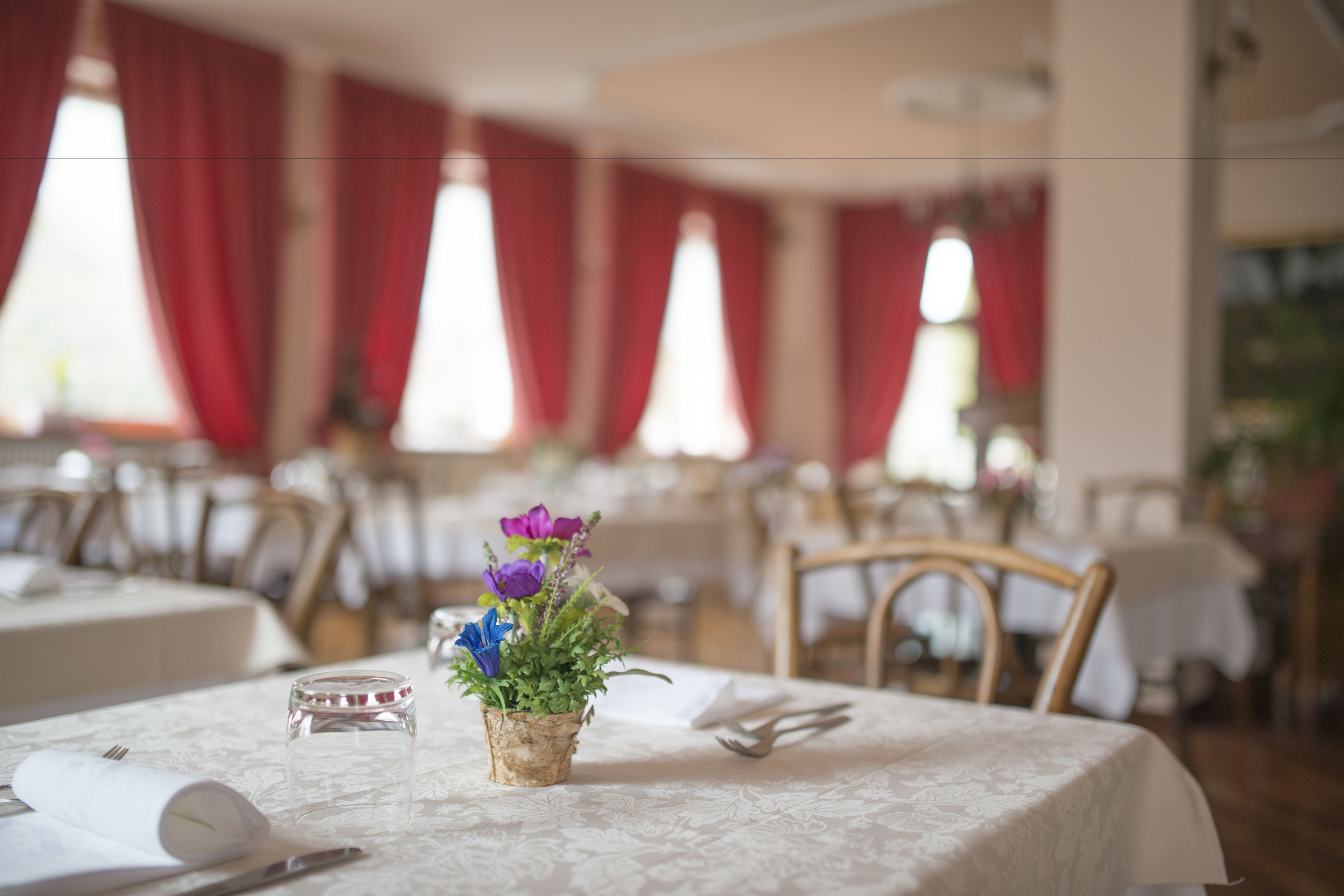 A dining table with a small vase of flowers, a folded napkin, and cutlery.