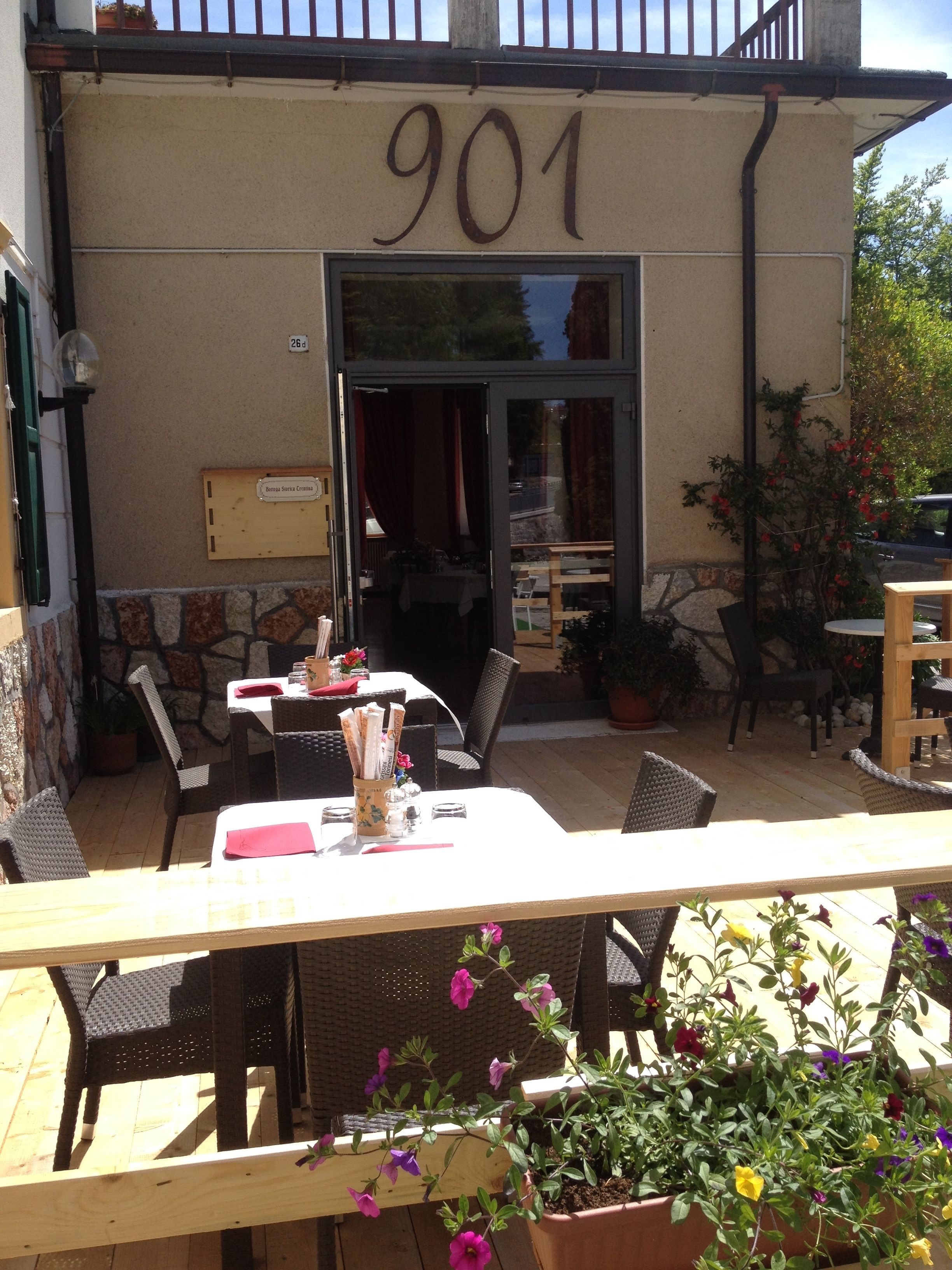 An outdoor cafe area with tables and chairs, a stone wall, and a door marked with the number 901.
