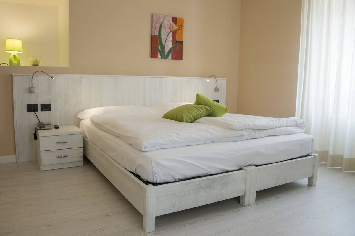 A modern bedroom with a white bed, green pillow, bedside table, and a wall-mounted lamp.