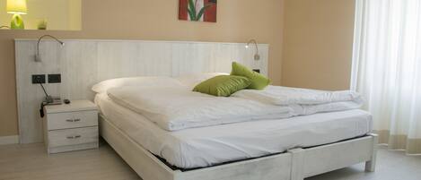 Un dormitorio moderno con cama blanca, almohada verde, mesita de noche y una lámpara de pared.