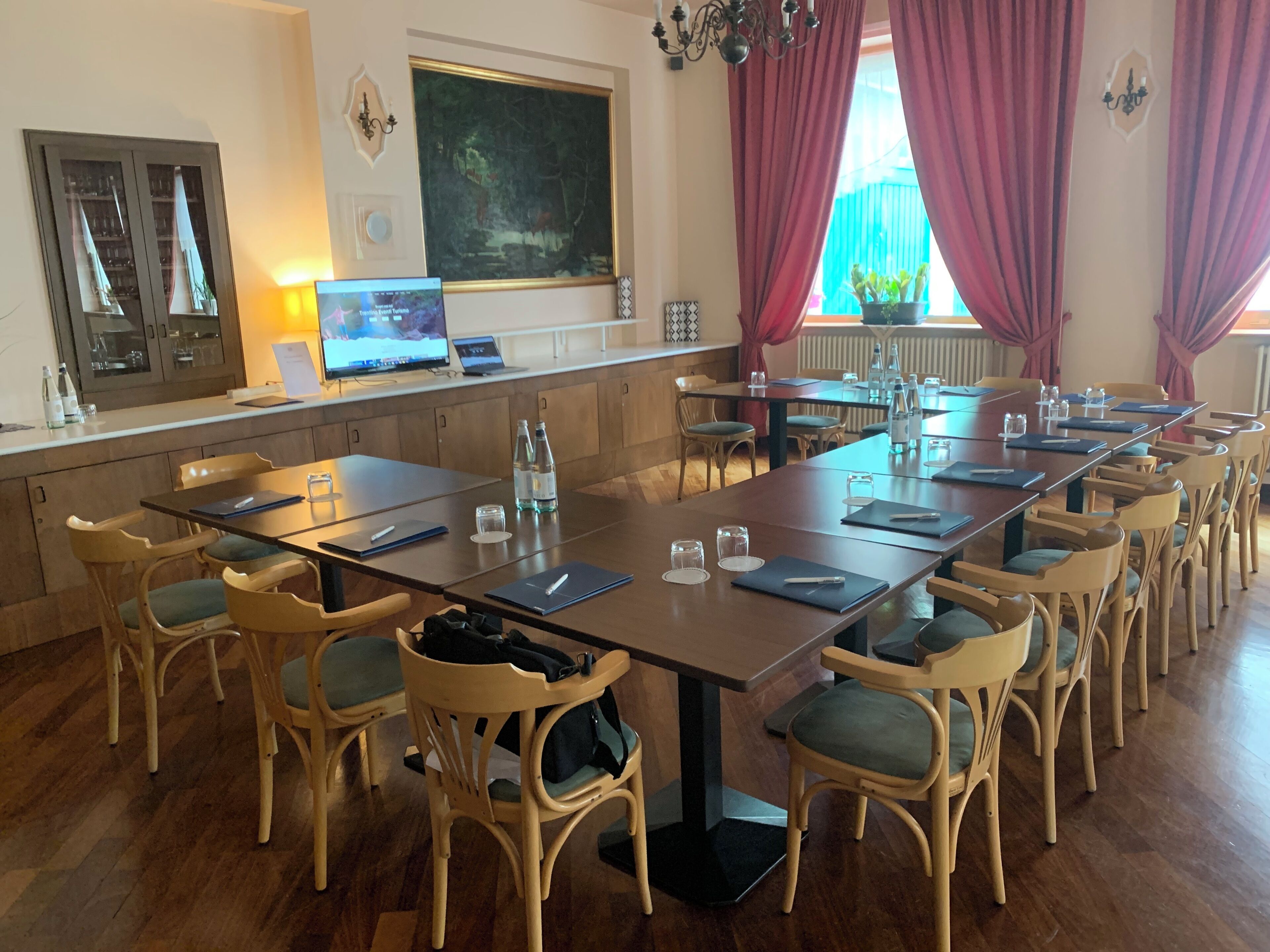 A conference room with a long table, multiple chairs, a laptop, and a large painting on the wall.