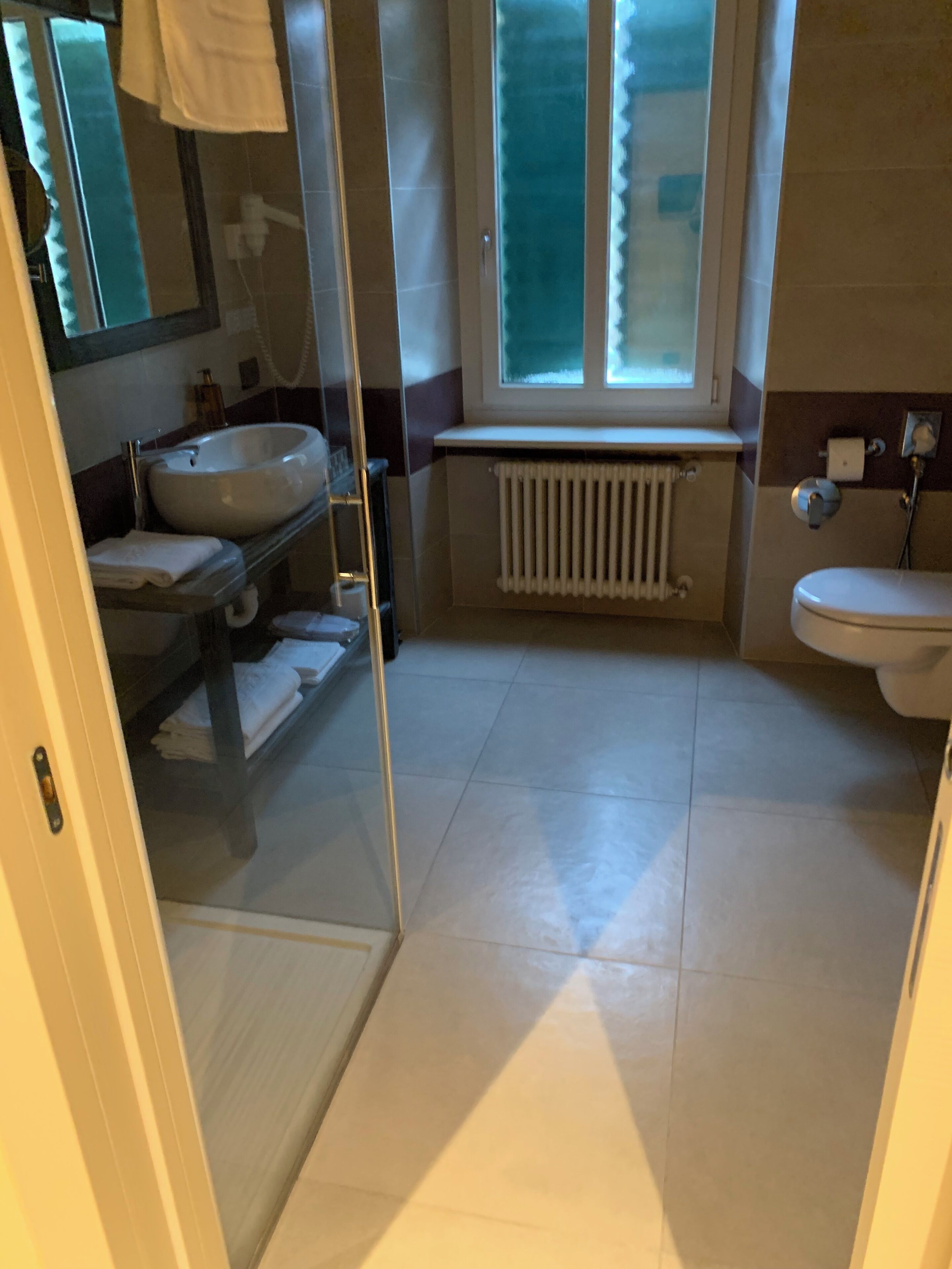 A bathroom with a glass shower door, a sink, a toilet, and a window.