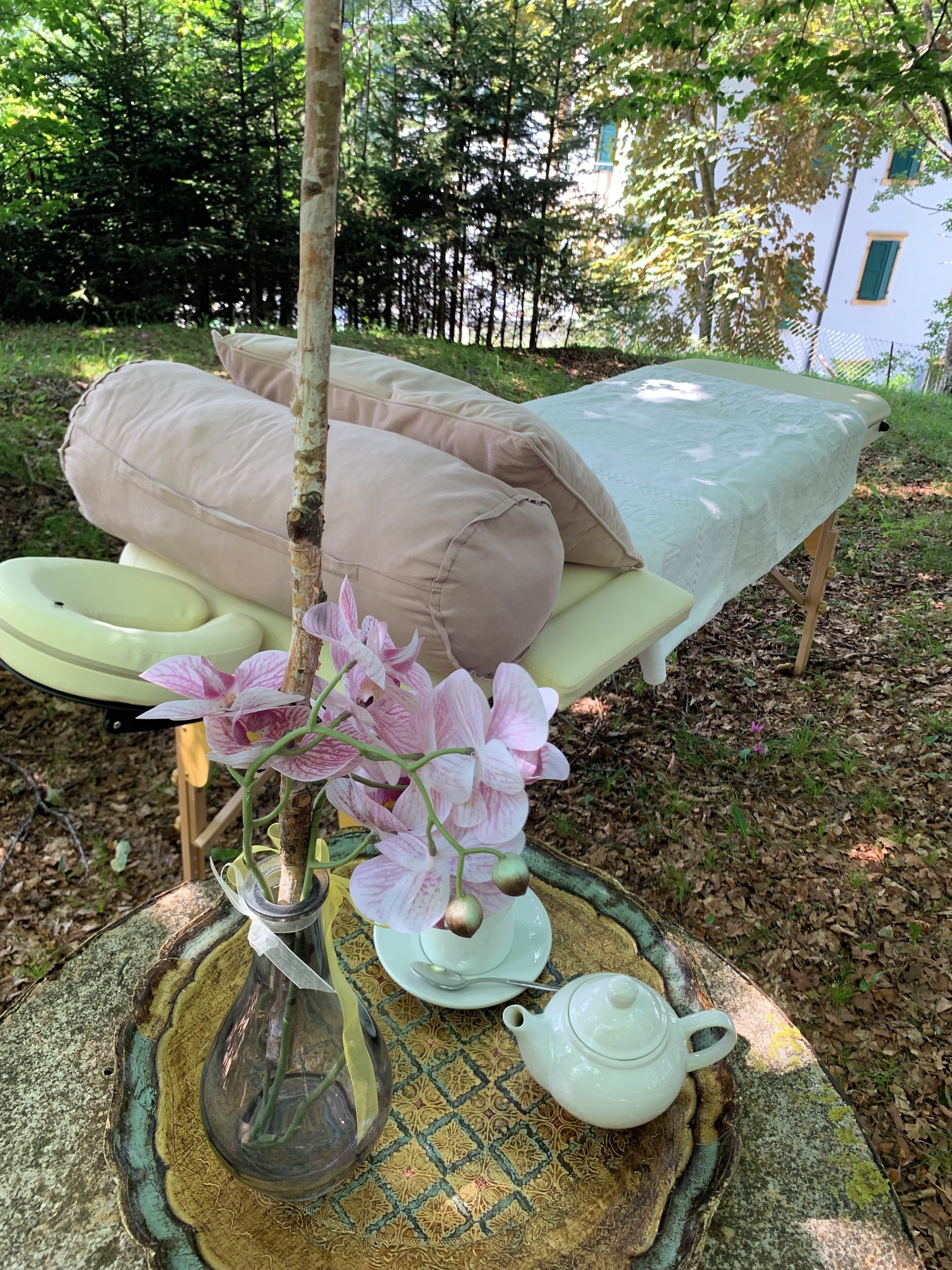 A cozy outdoor seating area with a table set for tea, surrounded by lush greenery.