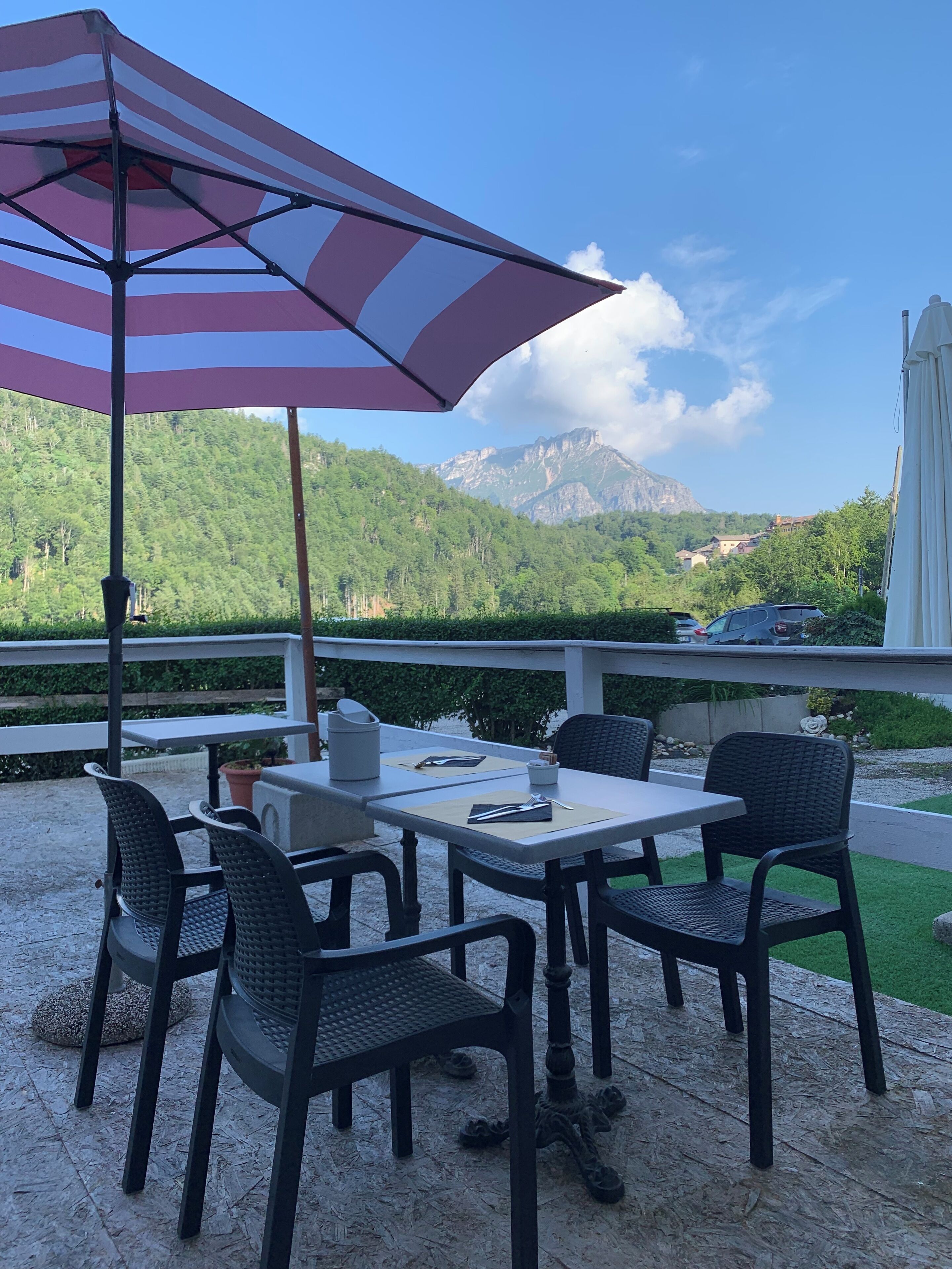 Eine Terrass mit Tisch und Stühlen, einem gestreiften Sonnenschirm und Blick auf Berge und Grün.
