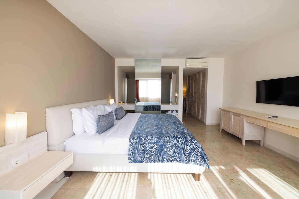 Una habitación de hotel moderna con una cama, mesitas de noche, un escritorio, un televisor y un baño visible a través de una puerta abierta.