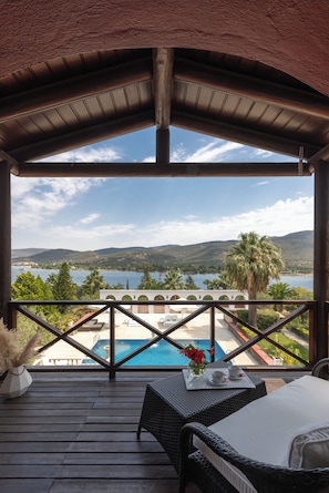 Un espacio al aire libre techado con vista a una piscina, una mesa con una bandeja de flores y una taza, y una silla de mimbre.