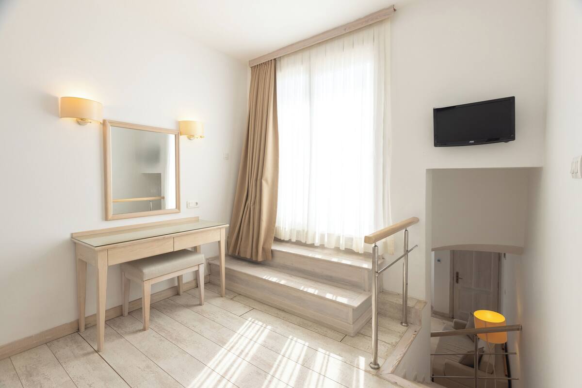 Habitación de hotel con un escritorio de madera, un espejo, un televisor y una escalera con barandilla.