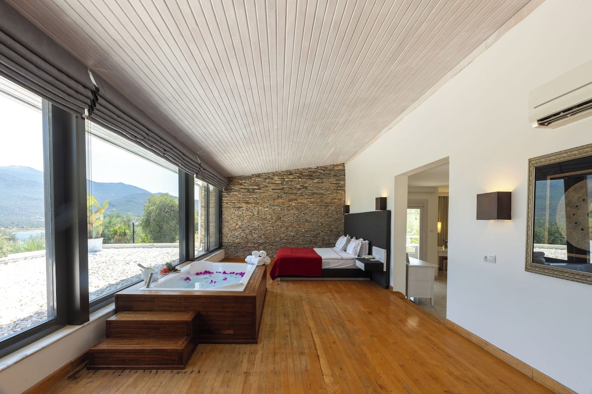 Un dormitorio moderno con pared de piedra, un ventanal grande, suelo de madera y una bañera empotrada.