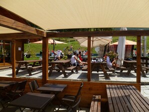An outdoor patio area with wooden tables and chairs, covered by a canopy. - Chalet del Sole (Sauze d'Oulx)