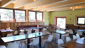 A restaurant with wooden tables and white chairs, large windows, and a green wall. - Chalet del Sole (Sauze d'Oulx)