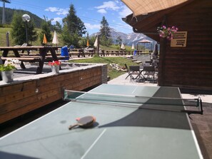 An outdoor ping pong table with a net, surrounded by wooden benches and potted plants. - Chalet del Sole (Sauze d'Oulx)