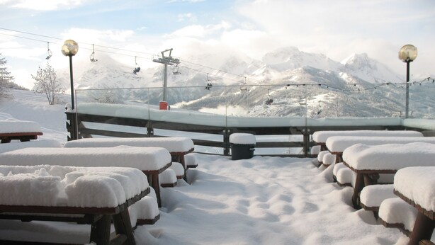 A snow-covered outdoor seating area with benches and tables, overlooking a ski slope with a chairlift and snow-covered mountains. - Chalet del Sole (Sauze d'Oulx)