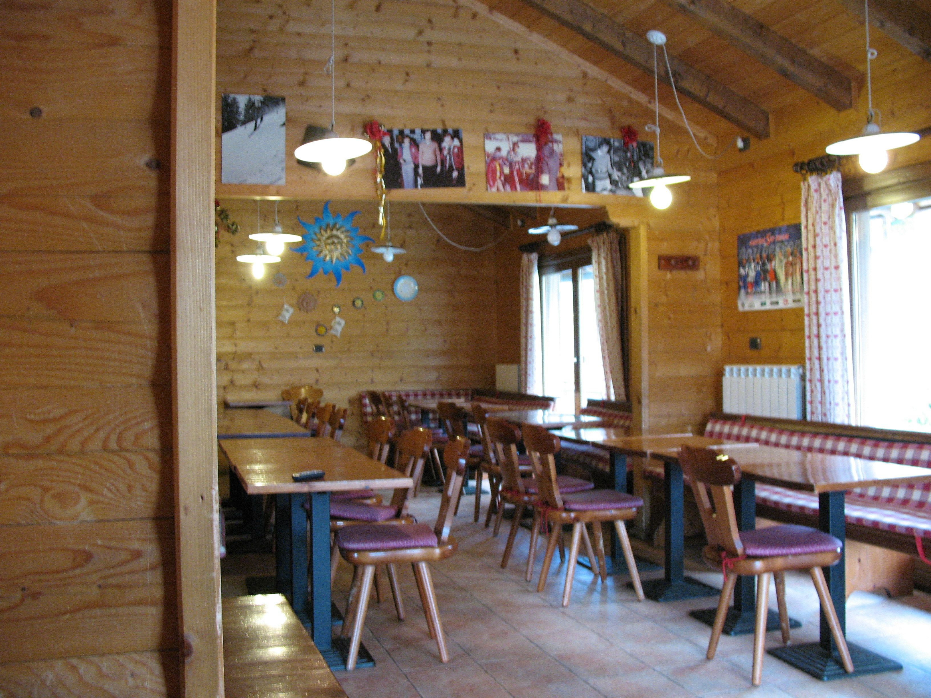 Un interno rustico in legno con diversi tavoli e sedie, una panca e un soffitto con travi a vista.