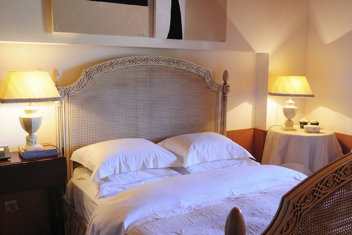 A neatly made bed with white linens, two bedside tables with lamps, and a decorative headboard.