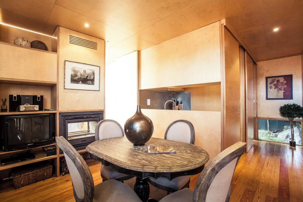 A cozy dining area with a round table, chairs, a television, and a fireplace.
