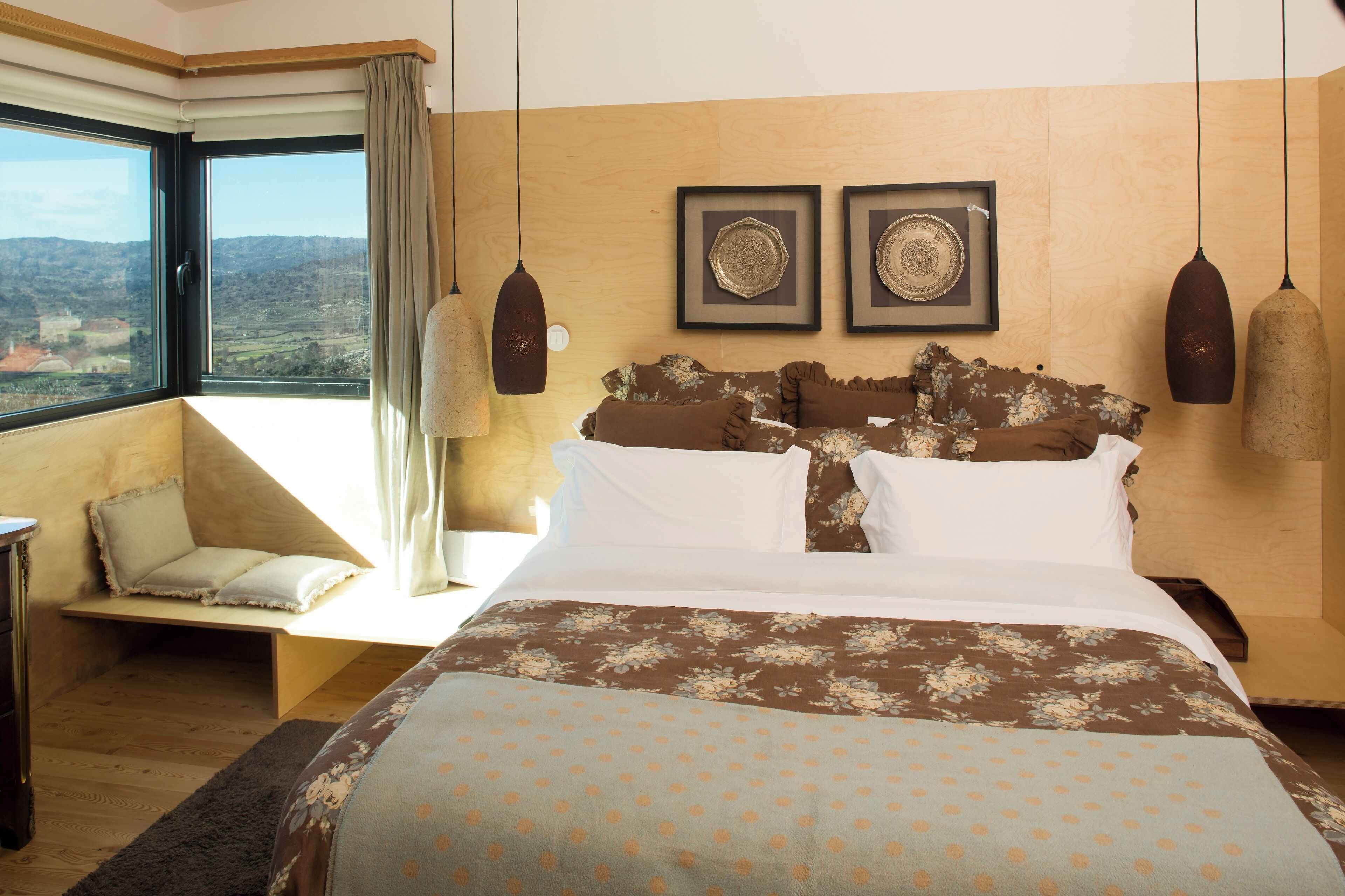 A bedroom with a large bed, a window with a view, and two framed pictures on the wall.