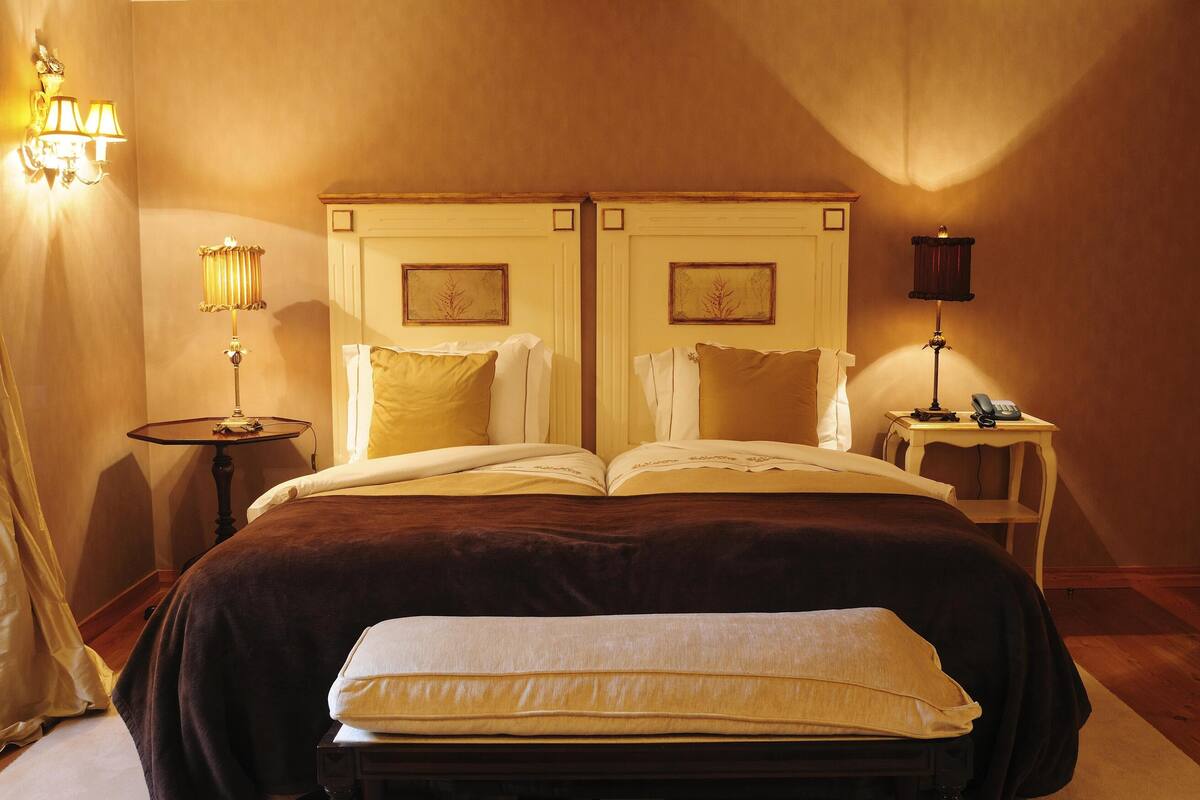 A double bed with a dark brown headboard, two bedside tables with lamps, and a small table with a lamp between the beds.