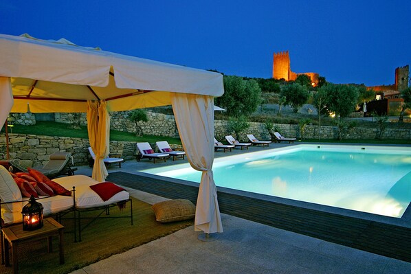 Un área junto a la piscina con sillones de descanso, una pérgola y una pared de piedra.