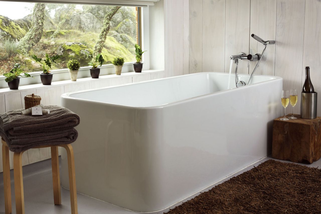 Un baño moderno con una bañera independiente, un taburete de madera con toallas, y vistas a la vegetación a través de la ventana.