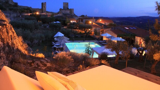 A pool area with umbrellas, a castle-like structure, and surrounding buildings. - Casas do Coro (Meda)