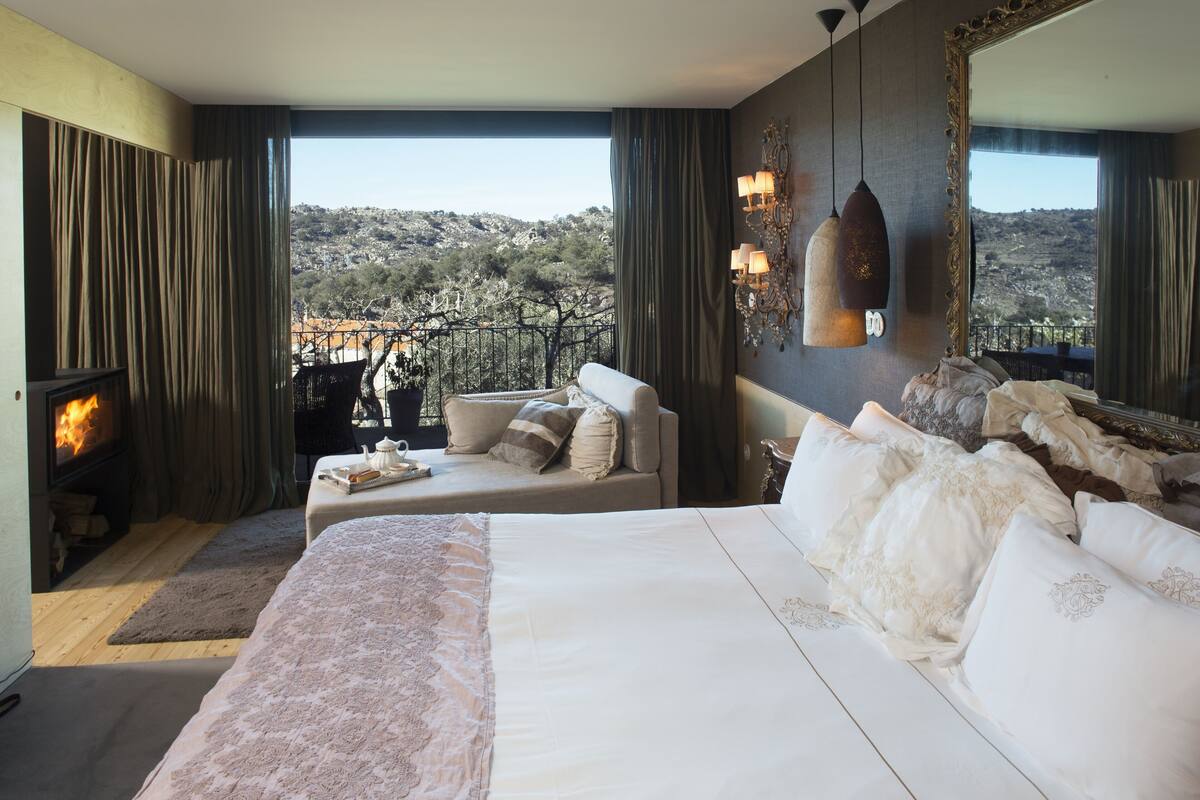 A bedroom with a large bed, a sofa, a fireplace, and a view of a mountainous landscape.