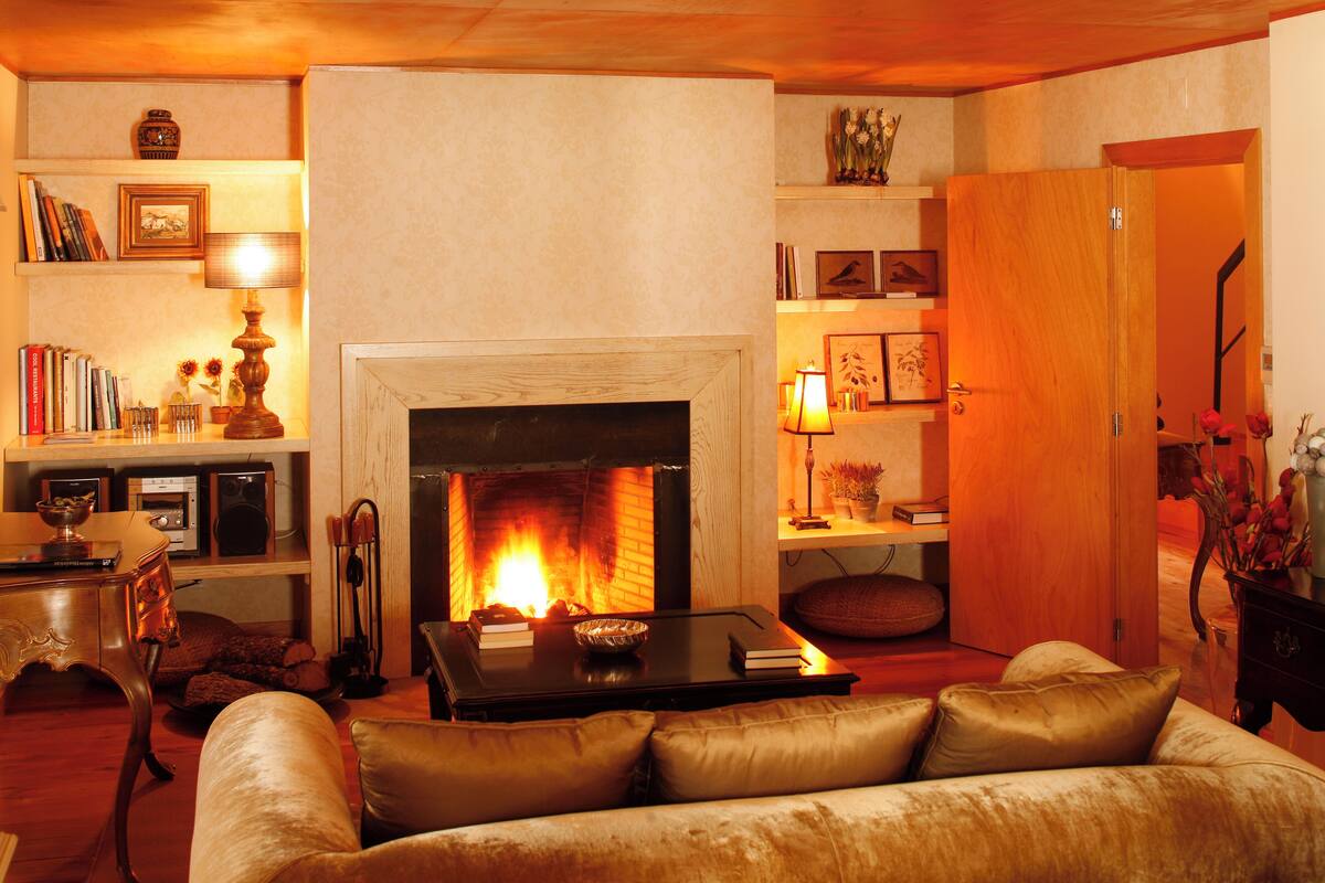 A cozy living room with a fireplace, leather sofa, bookshelves, and a wooden door.