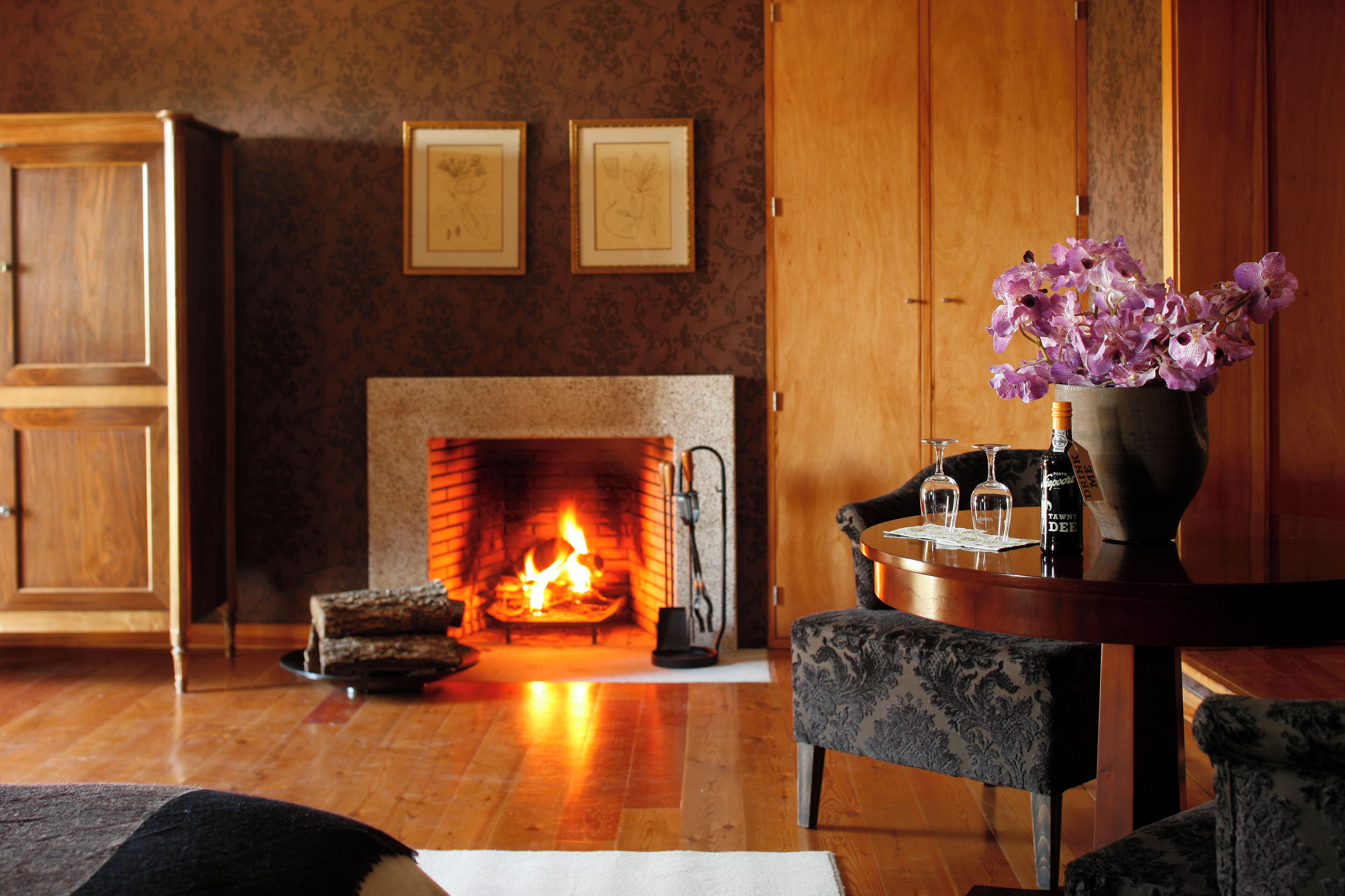 A cozy living room with a fireplace, a dining table with chairs, and a vase of flowers.