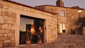 A stone building with a red-tiled roof, a large glass entrance, and a small window. - Casas do Coro (Meda)