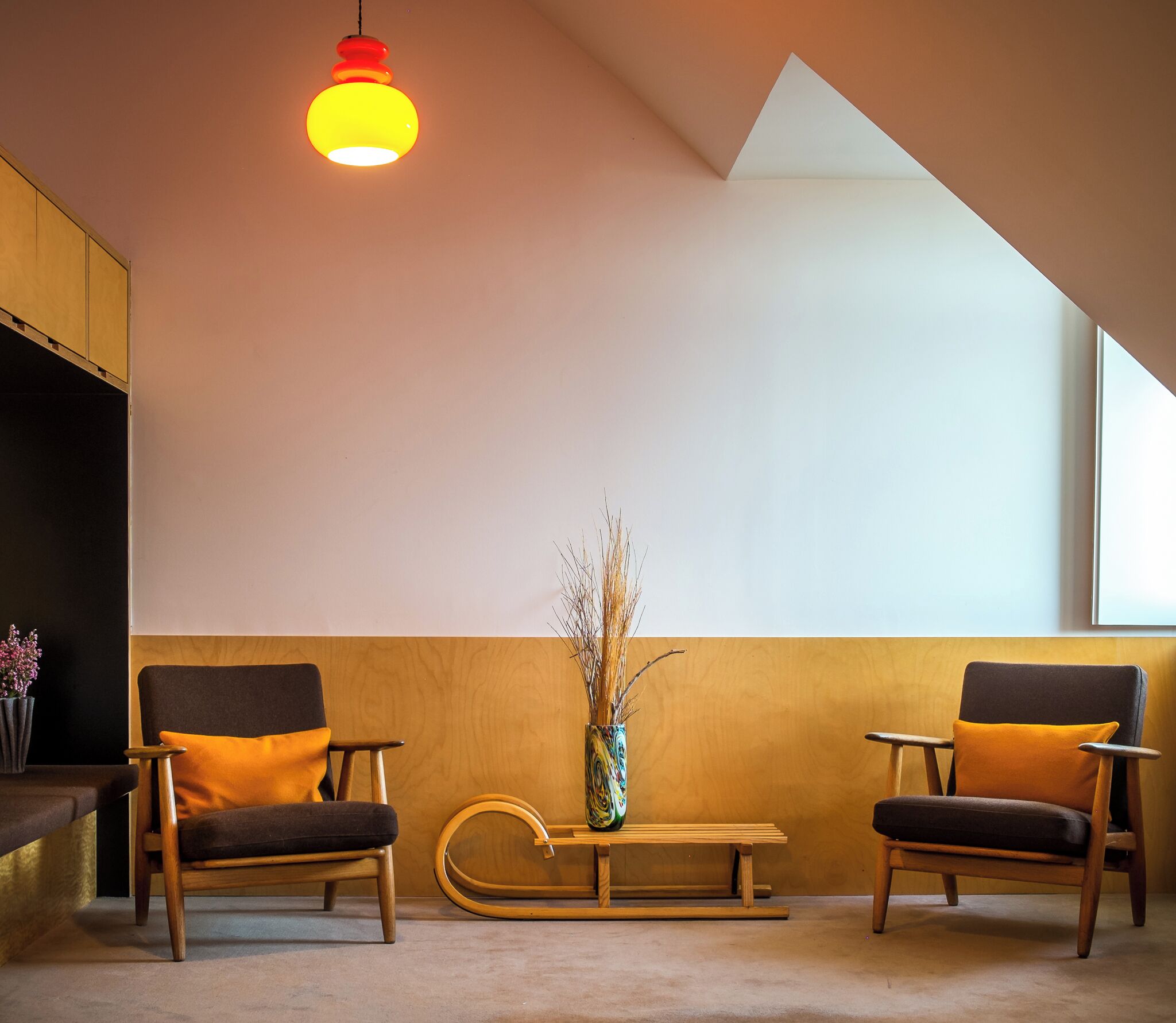 A modern interior with two chairs, a small table, a vase with branches, and a hanging light fixture.