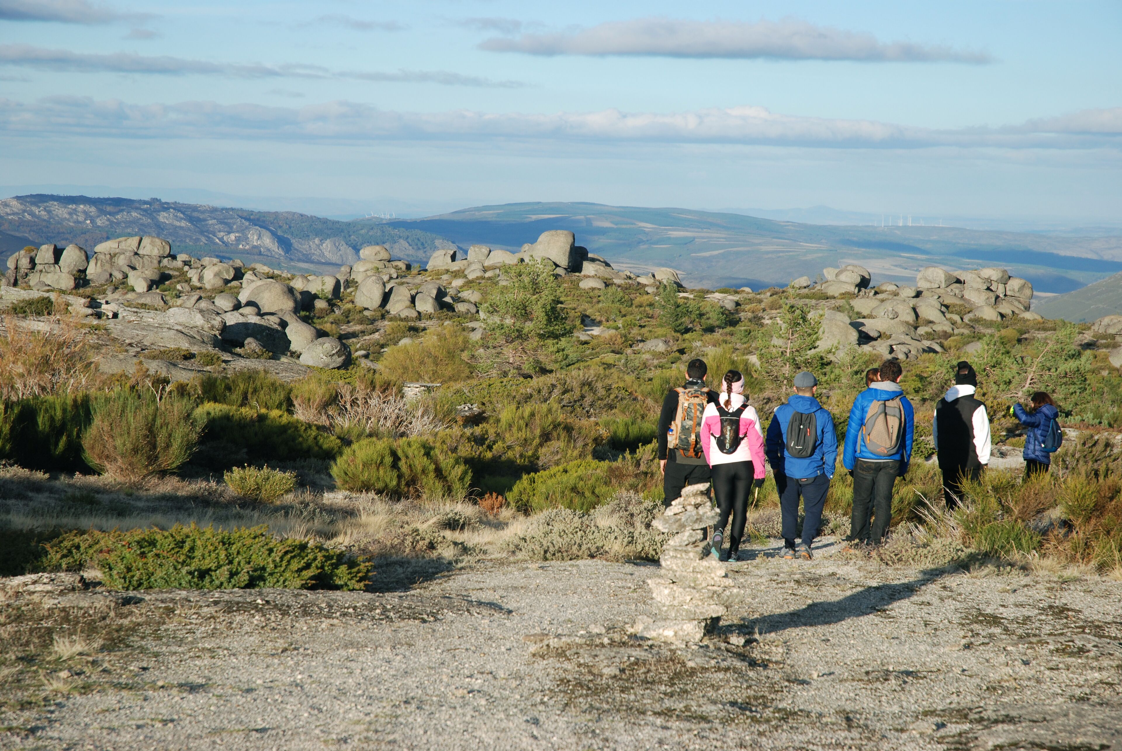 A group of hikers on a rocky trail with a view of distant wind turbines.