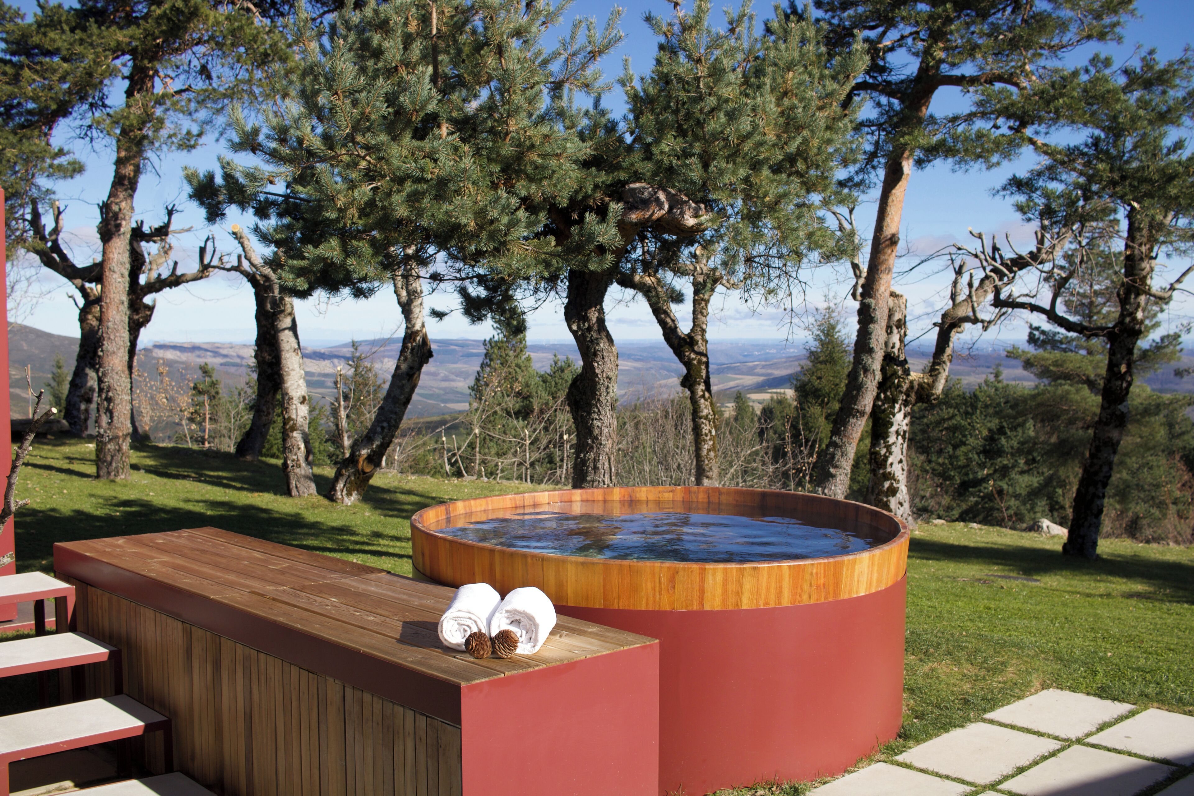 A hot tub with a wooden bench and towels, surrounded by trees and a view of the landscape.