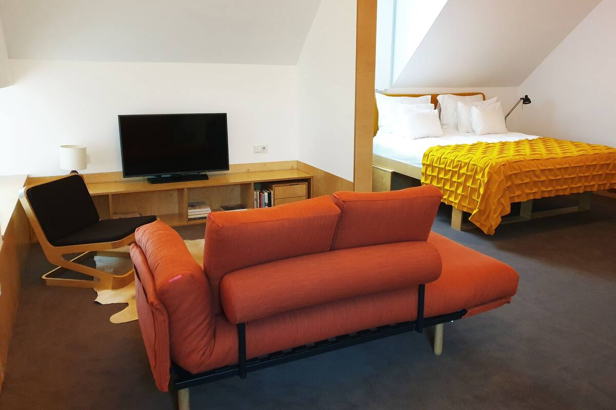 Ein modernes Zimmer mit einem Bett, einer Couch, einem Schreibtisch und einem Fernseher sowie einem Fenster.
