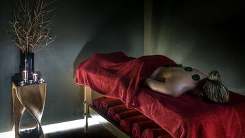 Sala de massagem com mesa de madeira, toalhas vermelhas e um vaso decorativo com galhos.