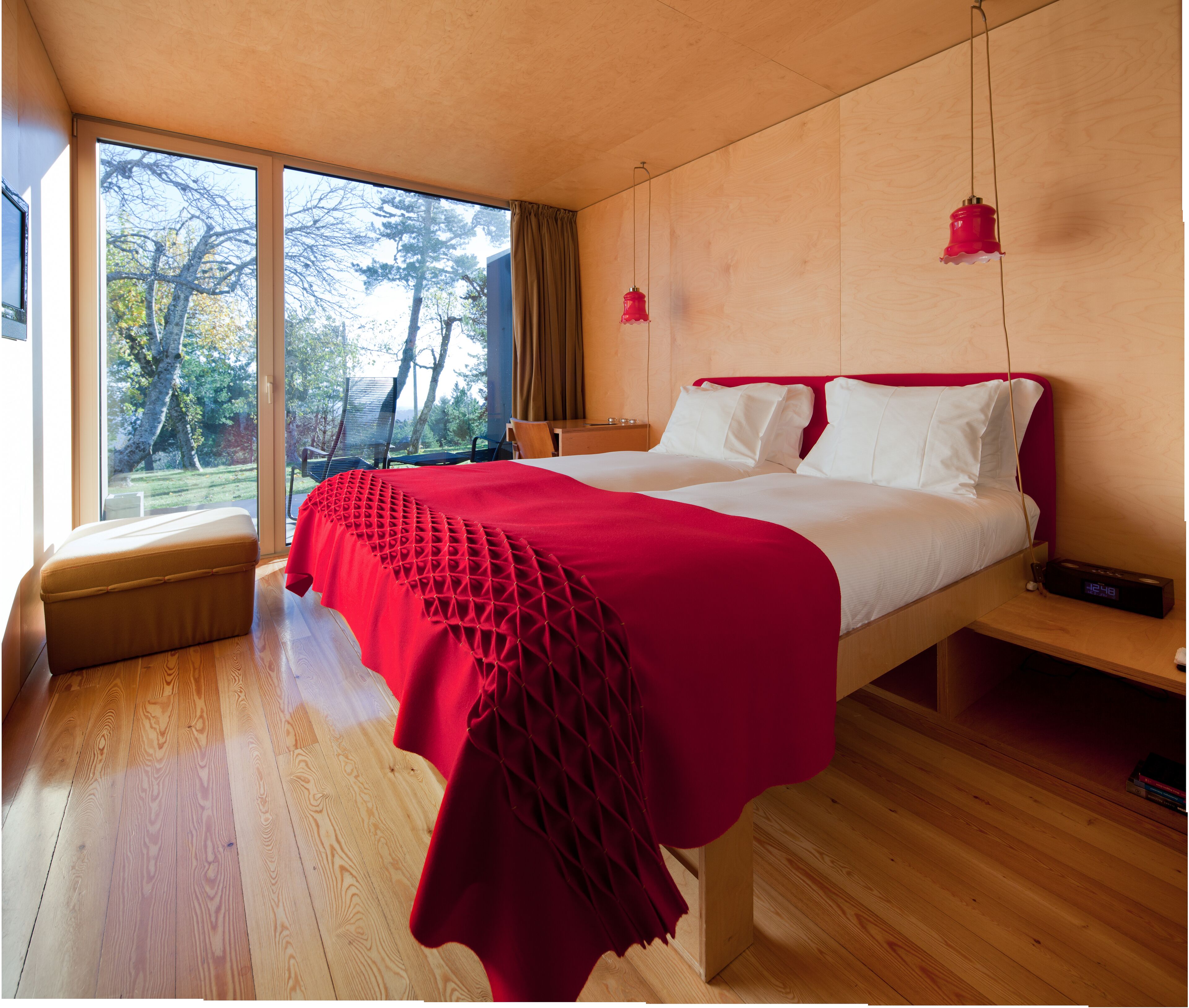 Un dormitorio moderno con una cama grande, suelo de madera y vistas a árboles por la ventana.