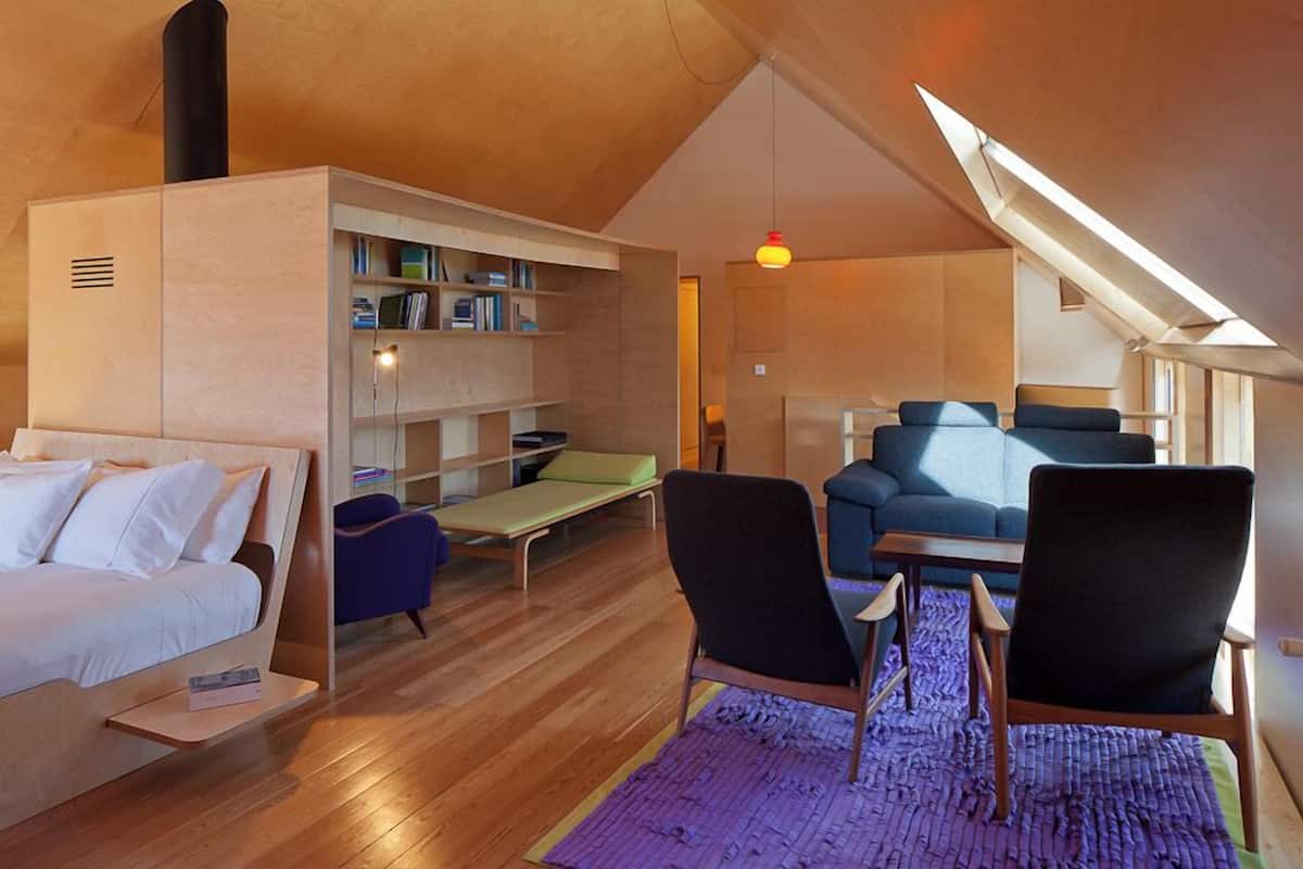 Ein gemütlicher Loft-Raum mit einem Bett, einer Sitzecke mit Tisch, einem Bücherregal und einem Dachfenster.