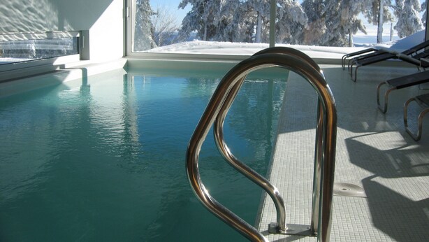 A pool with a metal railing, a tiled deck, and a view of snow-covered trees through a large window. - Casa das Penhas Douradas - Burel Expedition Hotel (Manteigas)