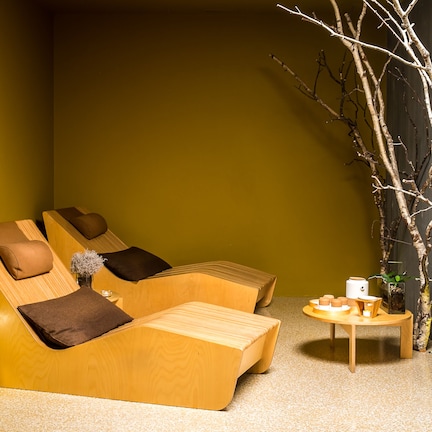 A modern relaxation area with wooden loungers, a small table with cups, and a decorative branch.