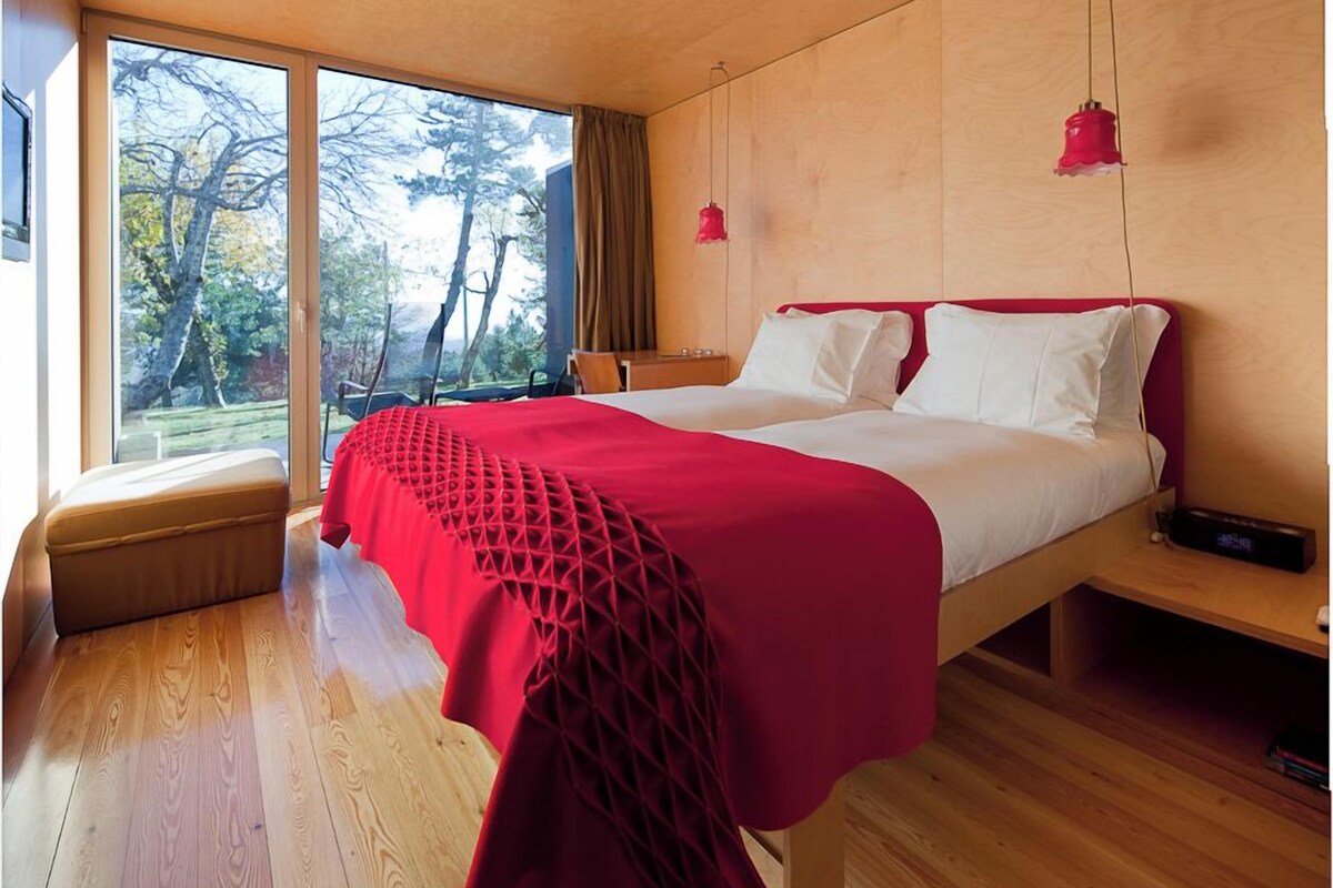 Une chambre moderne avec un grand lit, un plancher en bois et une vue sur les arbres par la fenêtre.