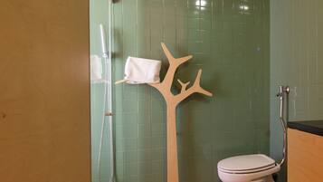 Een badkamer met een groene betegelde muur, een wit toilet, een douche met een glazen deur en een houten handdoekhouder in de vorm van een boom.