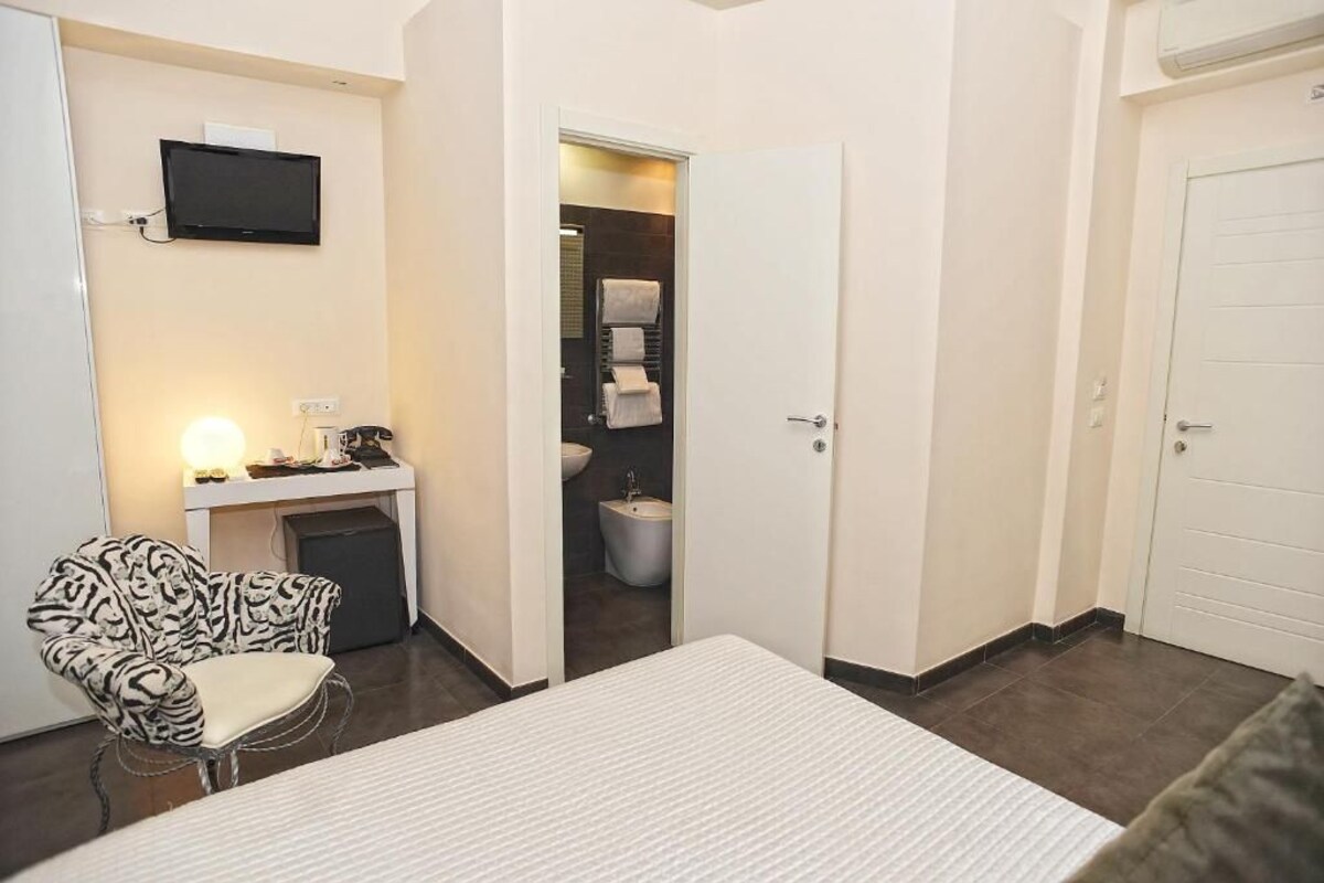 A hotel room with a bed, a desk with a chair, a television, and a bathroom visible through an open door.