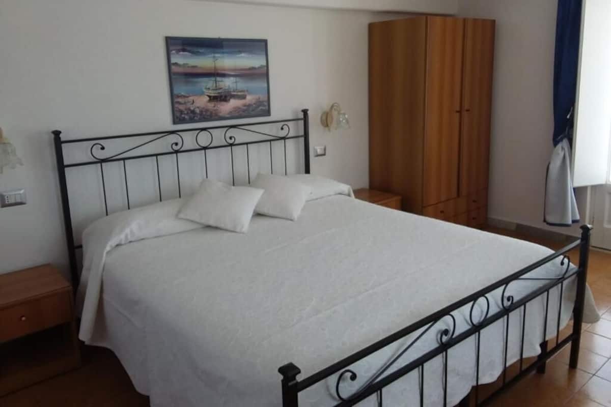 Ein Schlafzimmer mit Bett, einem Holzschrank, einem Bild an der Wand und einem Nachttisch.