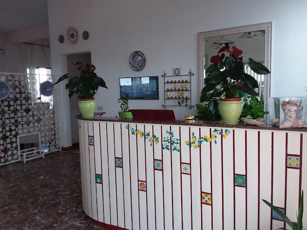 Un área de recepción con mostrador, plantas en macetas, un televisor y un adorno en la pared.